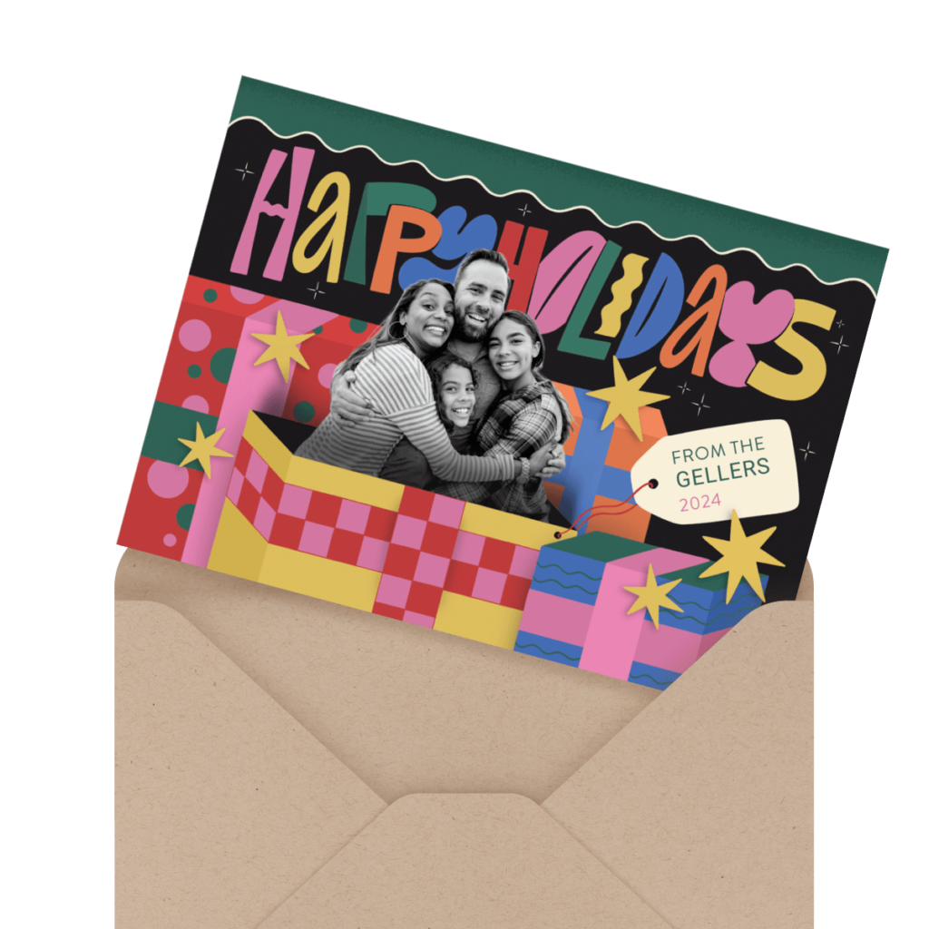 A holiday card with a family photo. Bright colors, stars, and gift box design. Text reads "Happy Holidays" and "From the Gellers 2024." Card is partially inside a brown envelope.