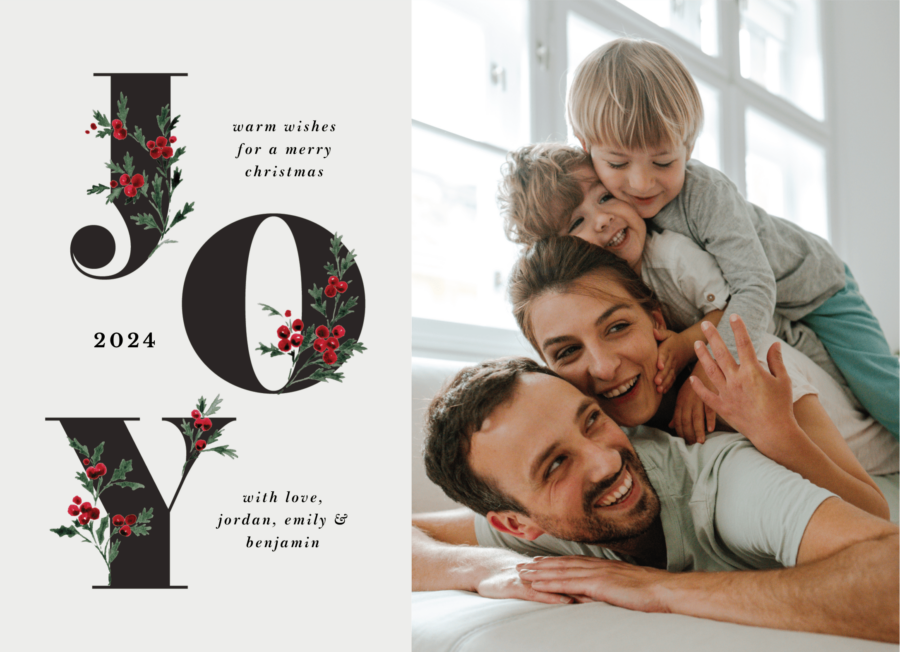 A family of four smiling and playing on a couch next to the word "JOY" decorated with holly. Text: "Warm wishes for a Merry Christmas 2024. With love, Jordan, Emily and Benjamin."