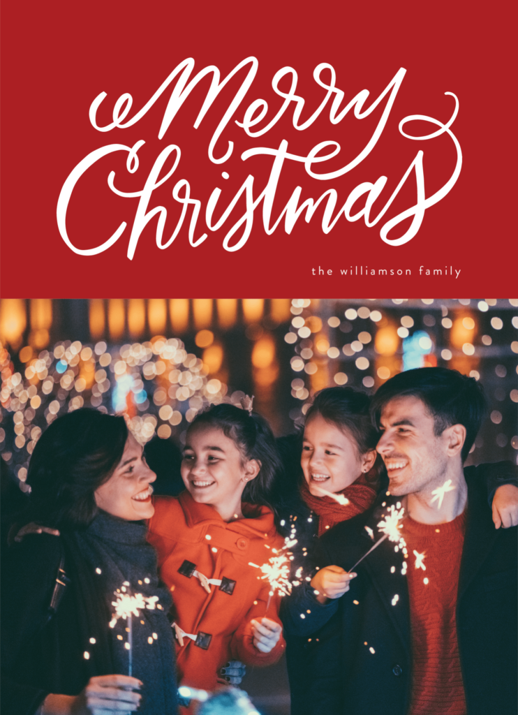 A joyful group of four people celebrate outdoors with sparklers, surrounded by festive Christmas lights.