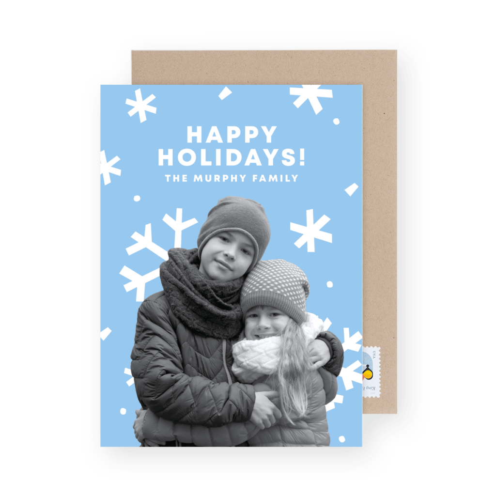 Holiday card featuring a black and white photo of two children in winter clothing hugging, with "Happy Holidays! The Murphy Family" text on a blue background with white snowflakes.