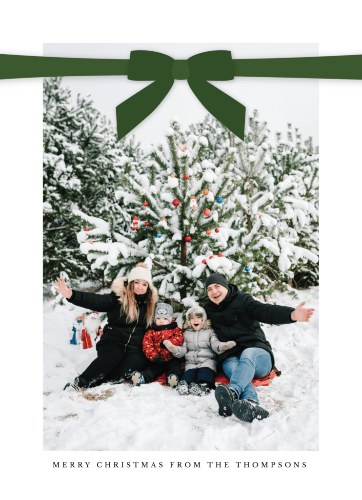 A family of four poses in front of a snow-covered Christmas tree outdoors, surrounded by snow.