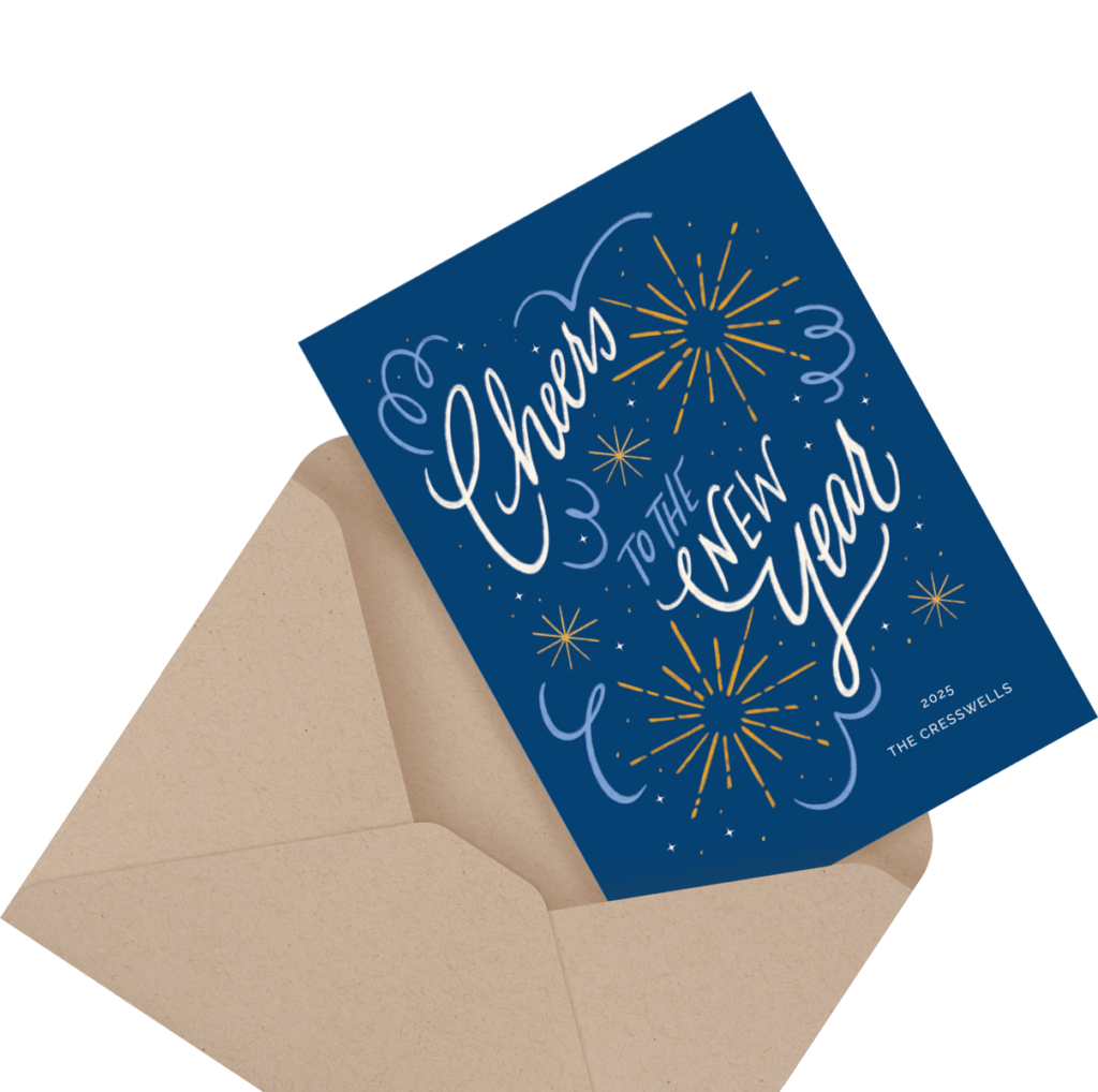 Blue New Year card with the text "Cheers to the New Year" surrounded by fireworks, partially inserted into a brown envelope.