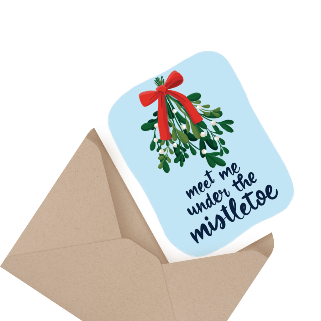 A greeting card with a mistletoe illustration and the text "meet me under the mistletoe," partially inserted into a brown envelope.