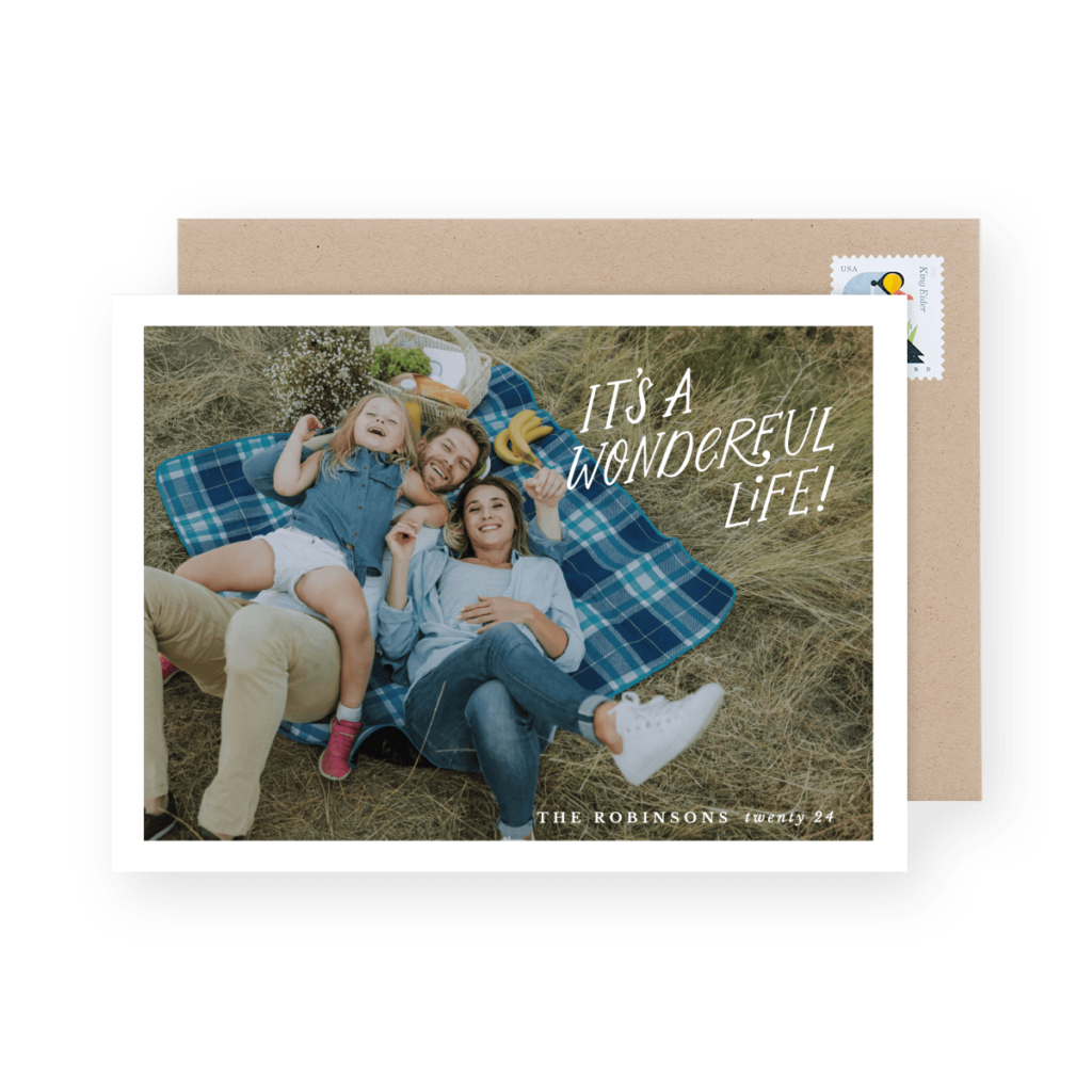 Family of four smiling and lying on a picnic blanket in a field. Text reads "It's a Wonderful Life!" along with "The Robinsons family '24."